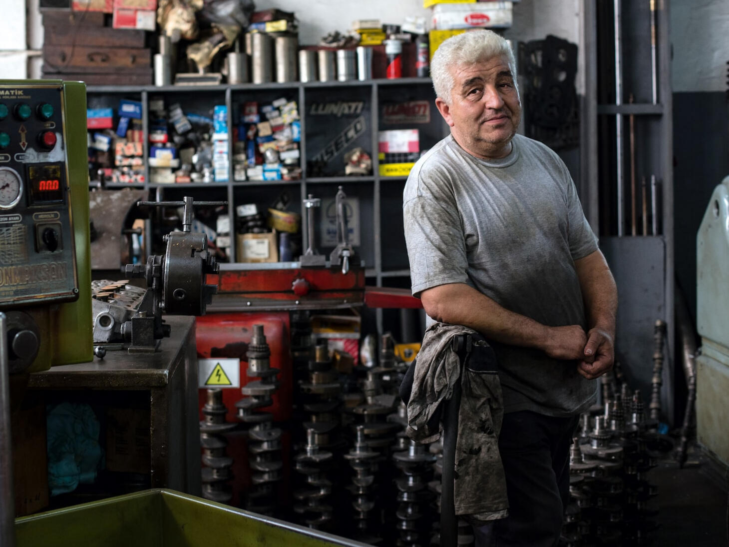 grease covered man in gray shirt with machinery beneath him in tool shop